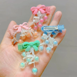 Detail of four colorful bow hair clips with acrylic beaded tassels on a person's hand