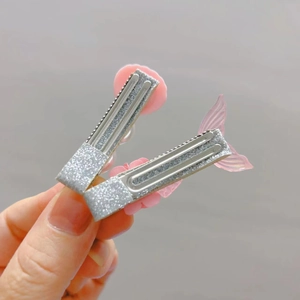 Detail view of two shiny silver hair clips with pink shell and mermaid tail designs
