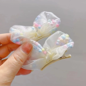 Dettaglio di due fermagli per capelli a fiocco in tulle bianco con pompon colorati