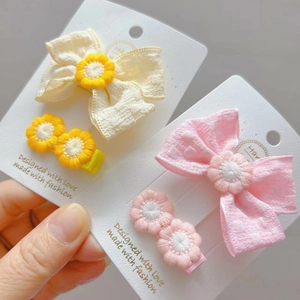 Dettaglio di fermagli per capelli a fiocco in tessuto giallo e rosa con fiori ricamati