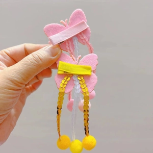 Détail de barrettes papillon avec ailes pailletées, glands et pompons jaunes