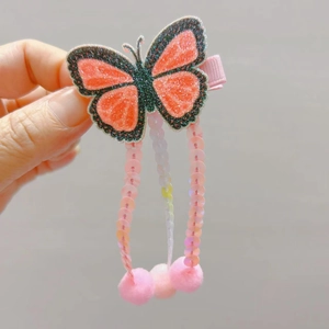 Détail de la pince à cheveux papillon pailletée avec pompons et pampilles roses