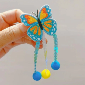 Détail macro d'une pince à cheveux papillon pailletée avec sequins et pompons colorés