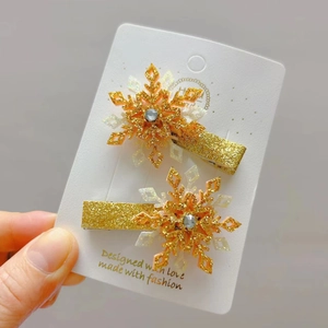 Détail de deux barrettes flocon dorées avec paillettes et strass sur une carte de support
