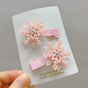 Détail de deux barrettes à cheveux flocon de neige rose pailleté avec strass sur carte