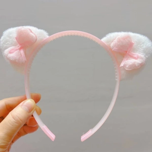 Détail d'un serre-tête oreilles de chat rose avec peluche blanche et petit nœud en soie