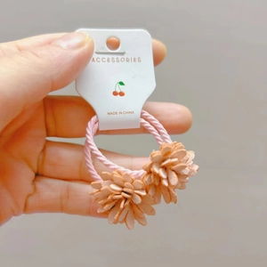 Détail de deux chouchous roses avec fleurs en tissu orange sur une carte en papier