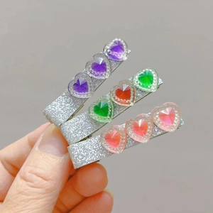 Close-up of three glittery hair clips with heart-shaped gems in purple, red, and pink colors