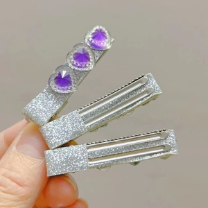 Close-up of three sparkling silver hair clips with purple heart-shaped gemstones