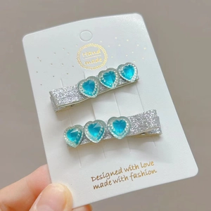 Detail of silver glitter hair clips with three blue resin hearts on white display card