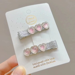 Macro shot of silver sequined hair clips with three pink heart-shaped crystal gems