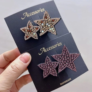 Detail showing two sparkling star-shaped hair clips with champagne and purple rhinestones