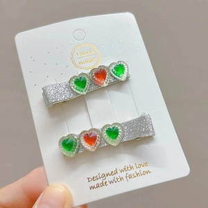 Detail view of handmade sparkling silver hair clips with green and red resin hearts