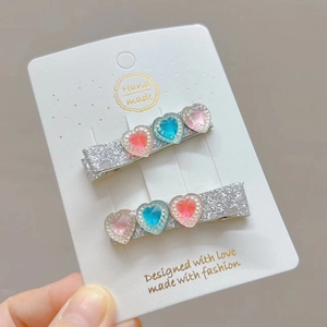 Close-up of handmade sparkling heart hair clips with pink and blue resin diamonds set on card