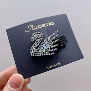 Detailed view of swan-shaped hair clip with white rhinestones and opal on jewelry card