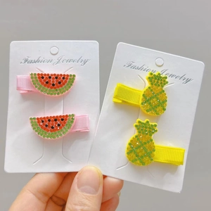 Close-up of handmade watermelon and pineapple hair clips with colorful rhinestones on a card