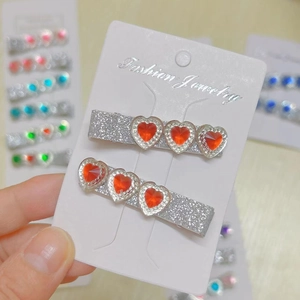 Close-up of silver glitter hair clips with three red heart-shaped rhinestones on a card