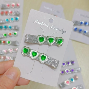 Close-up of two silver glitter hair clips with green heart-shaped gems on a display card