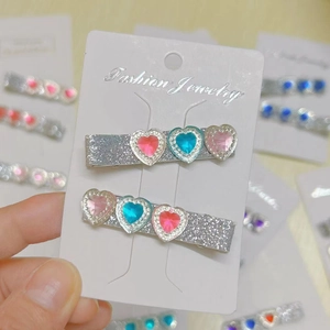 Close-up of glitter hair clips set with three colorful heart rhinestones on display card