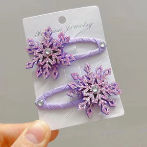 Dettaglio di due fermagli per capelli a fiocco di neve viola glitterati con strass su carta