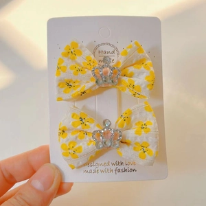 Gros plan de barrettes à nœuds en tissu avec motif floral jaune et breloque couronne