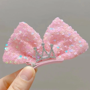 Detail einer rosa Haarschleife mit Pailletten und silberner Strasskrone in der Hand