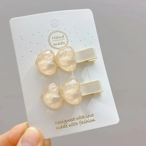 Dettaglio di due mollette per capelli a cuore color ambra con trama in resina su carta