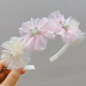 Dettaglio di fiori in tulle rosa e beige con perle a stella sul cerchietto per bimba
