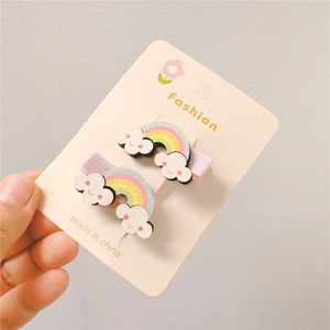 Glittering rainbow and cloud hair clips for kids on a card held by a hand