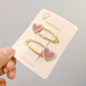 Close-up of heart-shaped hair clips with pink rhinestones and gold glitter finish