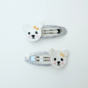 Detail of silver glitter hair clips featuring white embroidered bears with yellow bows