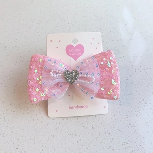 Barrette nœud rose à paillettes avec perles et ornement cœur sur carte de vente