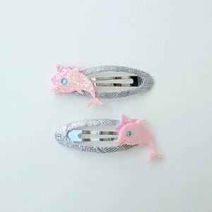 Detailed view of pink glitter dolphin hair clips with blue rhinestone eyes and silver bases