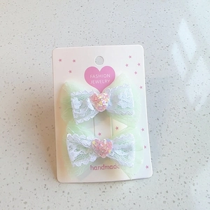 Detail view of light green mesh and white lace bow hair clips with pink glitter heart