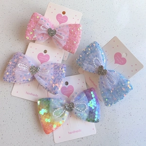 Détail de barrettes nœuds à paillettes avec perles et breloques cœur en plusieurs couleurs