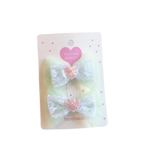 Pair of mint green lace bow hair clips with pink sequin heart on white display card