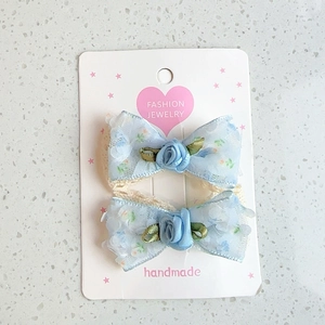 Detailed shot of light blue lace bow hair clips with satin roses and green leaves decoration