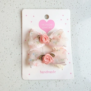 Detail of pink floral lace hair clips with handmade fabric roses on a display card
