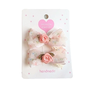 Pair of floral mesh bow hair clips with pink fabric roses on a white fashion jewelry card