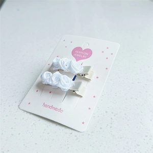 Détail de deux pinces à cheveux roses en satin blanc faites à la main sur carte de mode