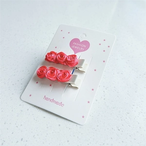 Détail de barrettes faites main avec roses en velours rouge sur carte de présentation
