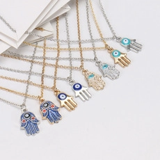 Detail of Hamsa Hand and Evil Eye pendants with gold and silver finishes on white card