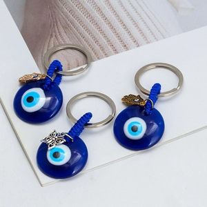 Detail of blue glass Evil Eye keychains with metal charms and woven cord on white background