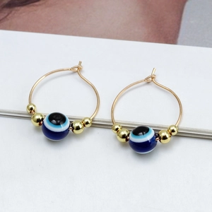 Detail of golden hoop earrings featuring blue Evil Eye beads and metallic accents