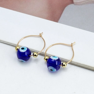 Macro detail of gold-tone hoop earrings with blue evil eye beads and metal spacers
