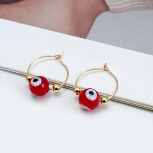 Close-up of golden hoop earrings featuring a red evil eye bead and small metal spacers