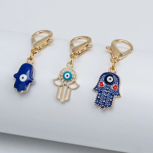 Trois pendentifs Main de Fatima avec œil porte-bonheur et fermoirs mousquetons dorés sur fond blanc