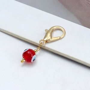 Détail d'un pendentif en verre œil grec rouge avec fermoir mousqueton doré et perles