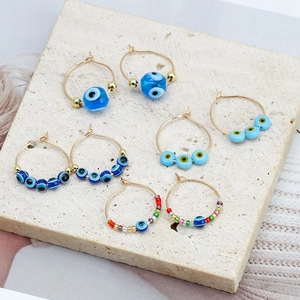 Detail of four pairs of gold evil eye hoop earrings with colorful beads on stone
