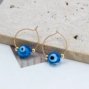 Gold evil eye hoop earrings with blue beads and colorful star charms on stone surface